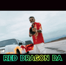 a man in a red shirt is holding a gun in front of a white car with a red dragon on the side