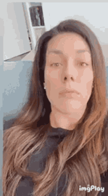 a woman with long hair is sitting on a couch and looking at the camera .