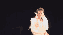 a man in a white jacket is singing into a microphone with his arms outstretched