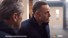 two men are standing next to each other in a hallway with the nbc logo on the bottom right