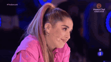 a woman in a pink shirt is sitting in front of a microphone and a masterchef logo