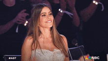 a woman in a white dress is sitting in front of a microphone with a sign that says #agt on it