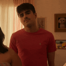 a man wearing a red polo shirt stands next to a woman in a room