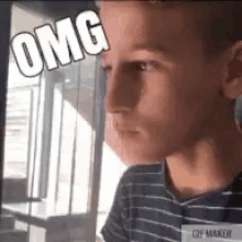 a boy in a striped shirt is looking out a window with the word omg written on his face .
