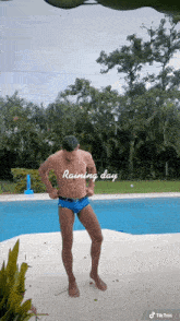 a shirtless man in blue swim trunks stands in front of a swimming pool