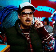 a man wearing sunglasses and a hat is talking on a cell phone in front of a sign that says county