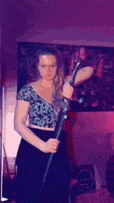 a woman in a crop top is holding a large sword in front of a purple wall .