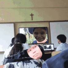 a group of people are sitting in front of a television with a cross above it