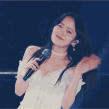 a woman with long black hair is holding a microphone in her right hand