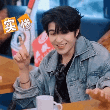 a man in a denim jacket is sitting at a table with a cup of coffee and smiling
