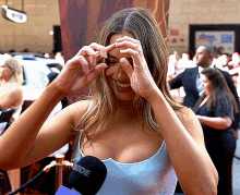 a woman in a blue tank top is smiling and holding her hands to her face