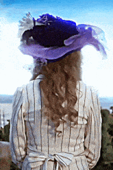 a woman wearing a striped shirt and a purple hat stands in front of the ocean