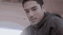a man with a beard and a hoodie is looking at the camera .