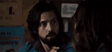a man with a beard is talking to a woman in front of a sign that says okay