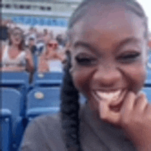 a woman is smiling while sitting in a stadium with her hand to her mouth .