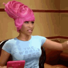a woman wearing a pink wig is sitting in a chair with her arms outstretched .