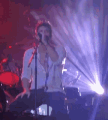 a man is singing into a microphone on a stage in front of a drum set .