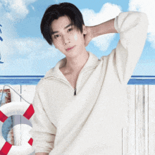 a young man in a white sweater stands in front of a life preserver on a beach