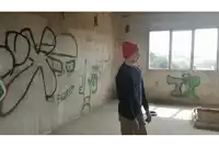 a man in a red hat stands in a room with graffiti on the walls including the word suc
