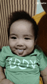 a baby wearing a green shirt that says daddy sticking out its tongue