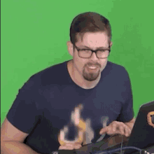 a man with glasses and a beard is sitting in front of a green screen .