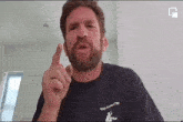 a man with a beard is wearing a black t-shirt and pointing his finger at something .