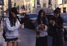 three girls are looking at their cell phones on a sidewalk in front of a building that says hollywood