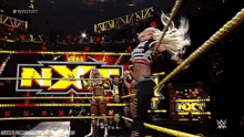a woman in a wrestling ring with the letters nxt on the wall behind her