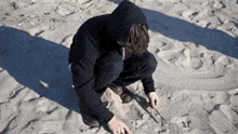 a man in a black hoodie is kneeling on a beach .