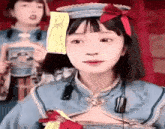 a girl is wearing a blue dress and a hat with a red bow and a sticky note on her head .