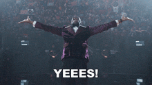 a man in a purple tuxedo is standing in front of a crowd with the words yeees behind him