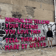 a man stands in front of a wall that says normalize telling your friends you love them