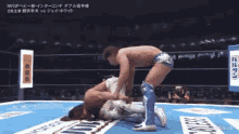 two men are wrestling in a wrestling ring and one of them is laying on the ground .