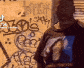a man wearing a shirt that says jimmy tim west is standing in front of a wall with graffiti on it .