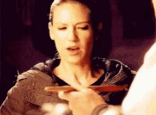 a woman is holding a piece of wood in her hand while looking at another person .