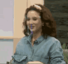 a woman wearing a denim shirt and a face shield is holding a straw in her mouth .