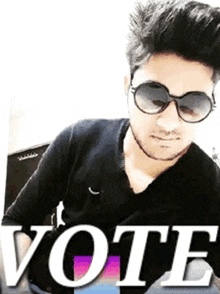 a man wearing sunglasses and a black shirt is standing in front of the word vote .