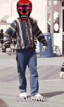 a man wearing a red skull mask and sunglasses is walking on a sidewalk .