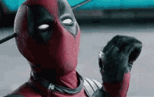 deadpool is wearing a red and black superhero costume and holding a sword .