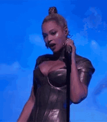 a woman is singing into a microphone on a stage in front of a blue sky .