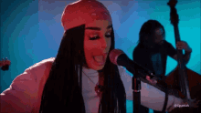 a woman is singing into a microphone in front of a man playing a bass .