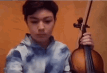 a young boy is playing a violin in front of a brown wall