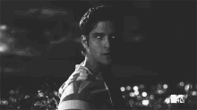 a black and white photo of a young man in a striped shirt standing in the dark .