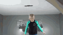 a young boy in a black and green shirt is jumping in the air in front of a chandelier