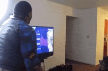 a man in a blue shirt stands in front of a flat screen television