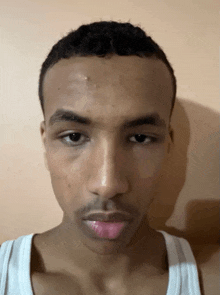 a young man with a beard and a white tank top looks at the camera