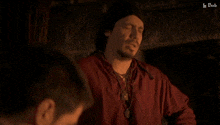 a man in a red shirt is talking to another man in a dark room with a caption that says " le bob "