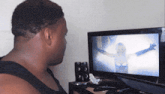 a man in a black tank top is looking at a television screen