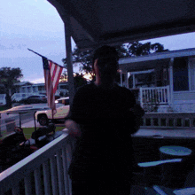 a man is standing on a porch with an american flag behind him
