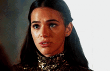 a close up of a woman 's face wearing a gold turtleneck and earrings .